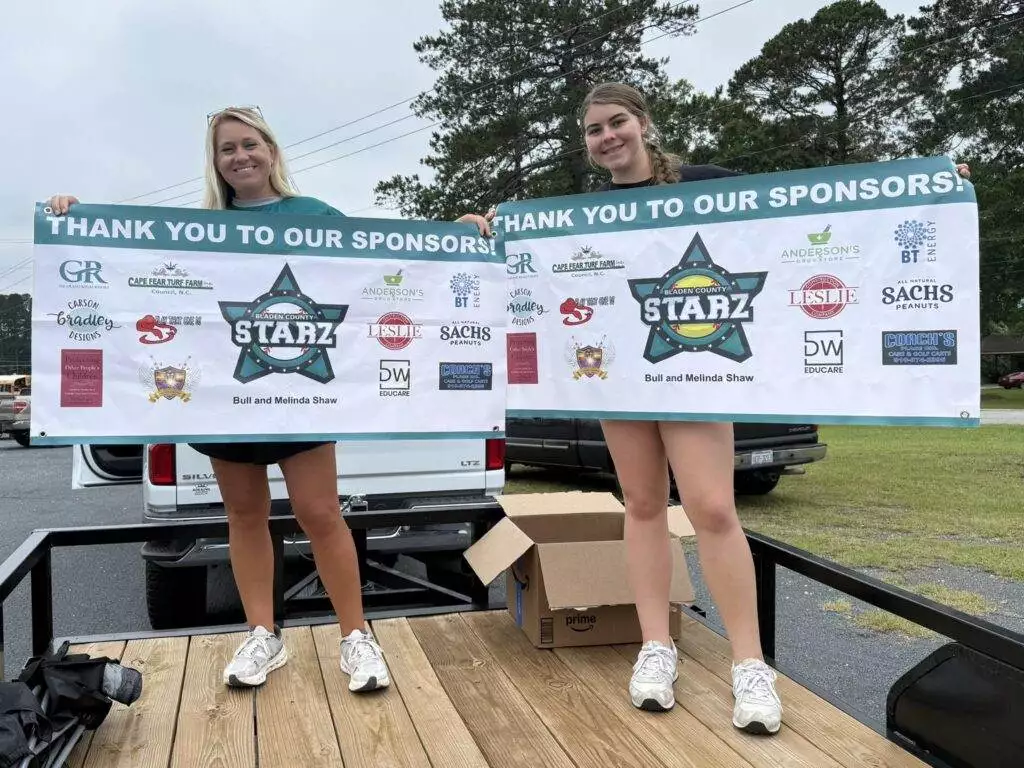 Coach Cara and Breelyn holding sponsor banners on trailer in parade.